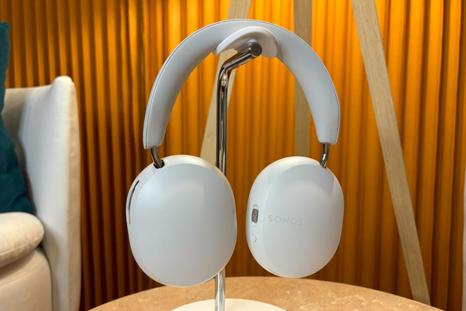 <p>White headphones on stand sitting on a small table, ear cups rotated to show the outside panel.</p>
