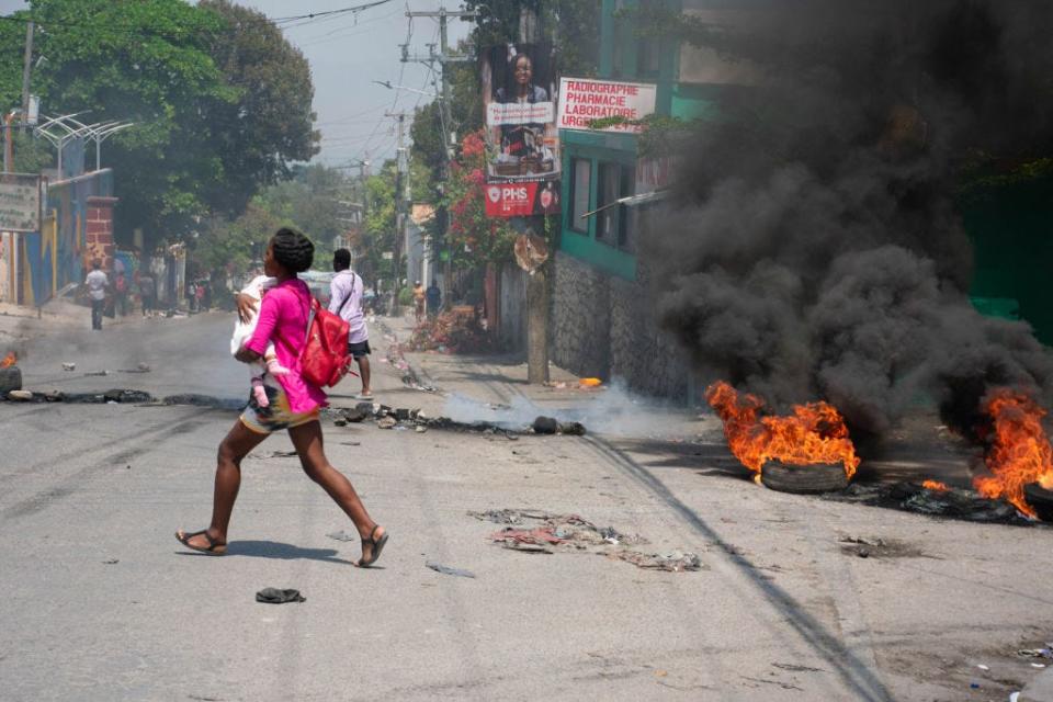 A woman carrying a child runs from the area after gunshots were heard in Port-au-Prince, Haiti, on March 20, 2024.