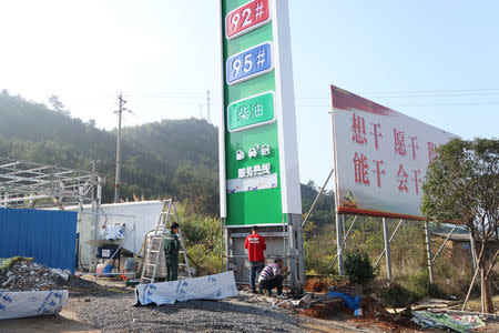 Men work at a gas station under construction next to a propaganda poster in Rucheng county, Hunan province, China December 3, 2018. Picture taken December 3, 2018. To match Insight CHINA-ECONOMY/DEBT-RUCHENG. REUTERS/Shu Zhang