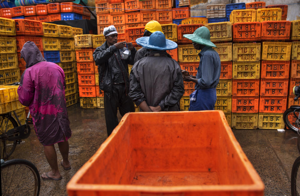 A man prepares to wear his mask as fish vendors chat on a rainy day in Kochi, Kerala state, India, Monday, June 22 2020. India is the fourth hardest-hit country by the COVID-19 pandemic in the world after the U.S., Russia and Brazil. (AP Photo/R S Iyer)