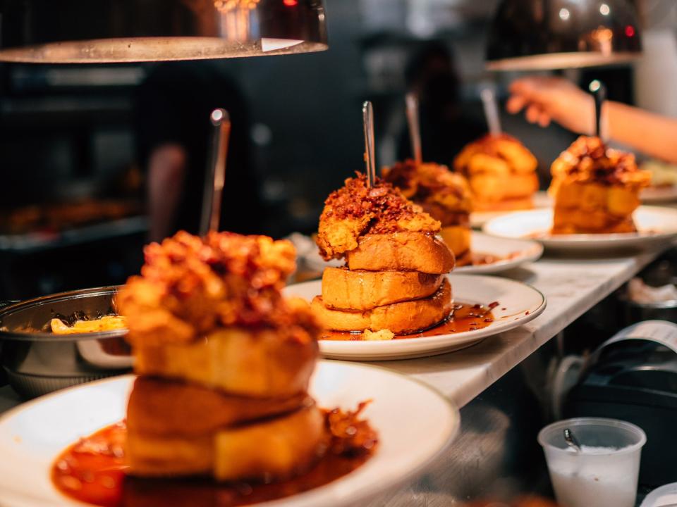 A photo of the hot honey chicken French toast at Maison Pickle, showing a row of plates of the French toast in the restaurant's kitchen.