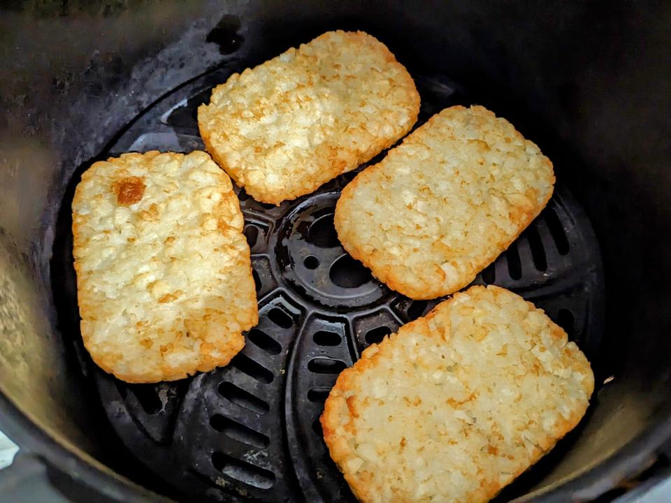 four hash brown patties in an air fryer basket