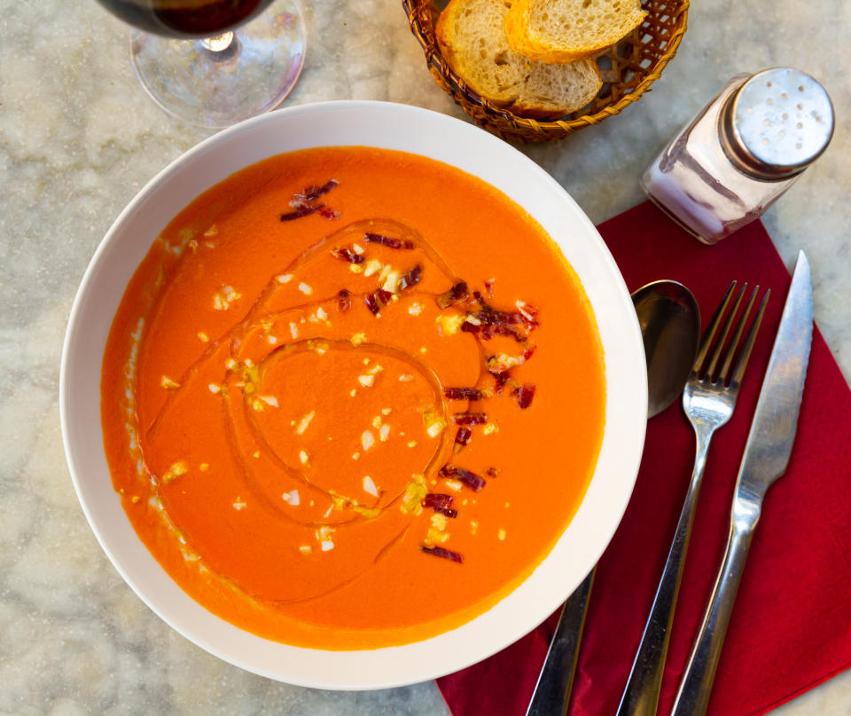 Bowl of creamy soup with bacon bits, on table with utensils and bread