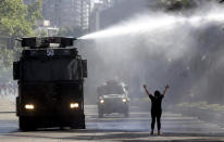 A protester holds her hands up toward a police truck spraying a water canon at students and union members marching in Santiago, Chile, Monday, Oct. 21, 2019. Hundreds of protesters defied an emergency decree and confronted police in Chile’s capital on Monday, continuing disturbances that have left at least 11 dead and led the president to say the country is “at war.” (AP Photo/Miguel Arenas)