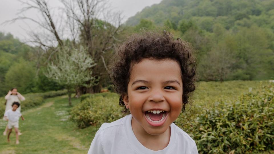 a black boy with an afro hairstyle walks among the tea plantations with his young asian mother, looks at the camera and makes faces