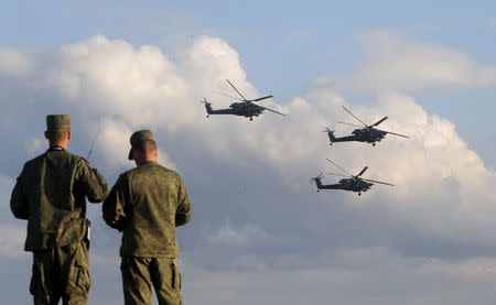 Russian servicemen watch Mi-28 military helicopters of the Berkuti (Golden Eagles) aerobatic team fly during the opening of the Army-2015 international military forum in Kubinka, outside Moscow, Russia, June 16, 2015. REUTERS/Maxim Shemetov