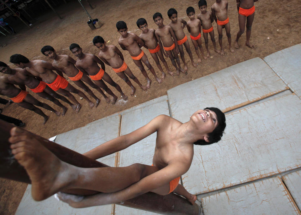 A boys perform a Mallakhamb pose on a pole as others watch at the Shree Samartha Vyayam Mandir in Mumbai