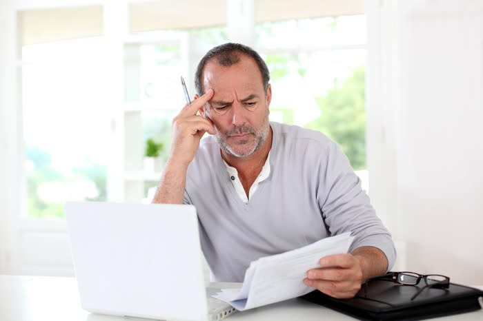 Man sitting in front of a computer, staring at papers, and appearing confused.