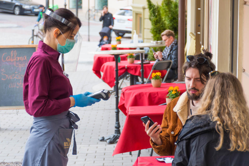 Waitress with a mask and clients at an outdoor bar, café or restaurant, reopen after quarantine restrictions