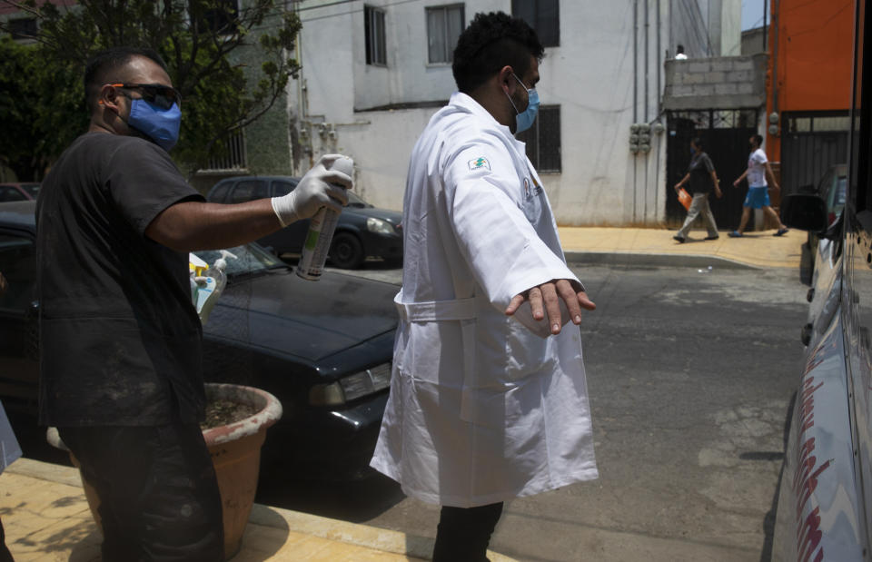 A health worker disinfects a fellow colleague after outside the home of a 75-year-old resident who they tested for COVID-19, in Mexico City, Wednesday, June 17, 2020. (AP Photo/Marco Ugarte)