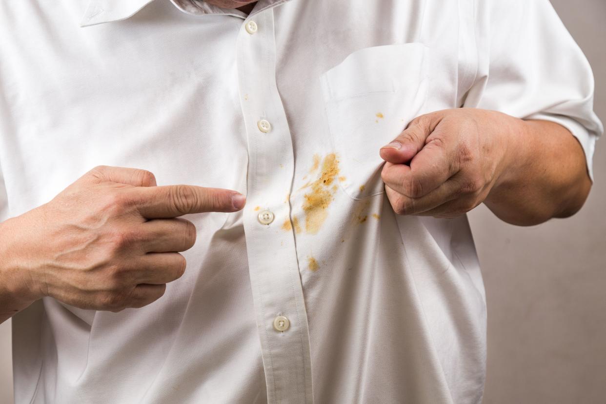 Frustrated man's finger pointing to spilled curry stain on white shirt, showing only torso with white shirt on and hands of man