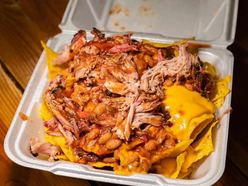 nachos topped with cheese and pulled pork in a styrofoam takeout container