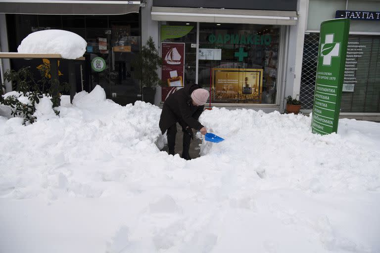 Una mujer quita la nieve afuera de una farmacia en Cholargos, suburbio de Atenas, después de una tormenta de nieve, el martes 25 de enero de 2022