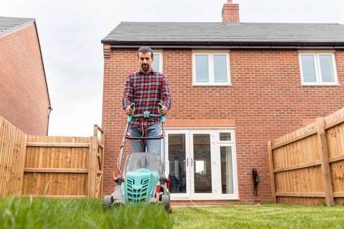 Mid adult man using lawn mower for mowing at backyard