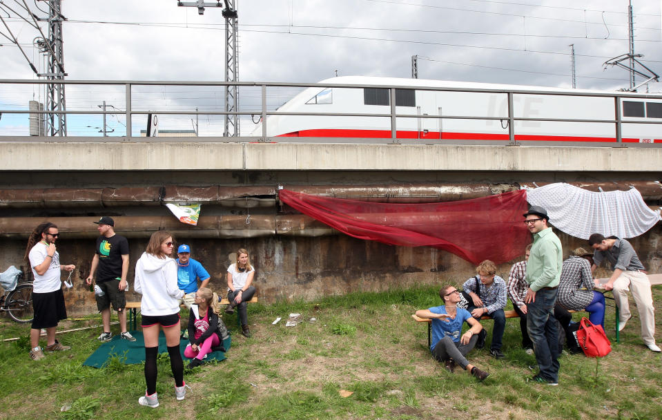 BERLIN, GERMANY - JULY 21: Attendees wait for the start of the games as a Deutsche Bahn ICE (InterCity Express) train passes overhead at the second annual Hipster Olympics on July 21, 2012 in Berlin, Germany. With events such as the "Horn-Rimmed Glasses Throw," "Skinny Jeans Tug-O-War," "Vinyl Record Spinning Contest" and "Cloth Tote Sack Race," the Hipster Olympics both mocks and celebrates the Hipster subculture, which some critics claim could never be accurately defined and others that it never existed in the first place. The imprecise nature of determining what makes one a member means that the symptomatic elements of adherants to the group vary in each country, but the archetype of the version in Berlin, one of the more popular locations for those following its lifestyle, along with London and Brooklyn, includes a penchant for canvas tote bags, the carbonated yerba mate drink Club Mate, analogue film cameras, an asymetrical haircut, 80s neon fashion, and, allegedly, a heavy dose of irony. To some in Berlin, members of the hipster "movement" have replaced a former unwanted identity in gentrifying neighborhoods, the Yuppie, for targets of criticism, as landlords raise rents in the areas to which they relocate, particularly the up-and-coming neighborhood of Neukoelln. (Photo by Adam Berry/Getty Images)