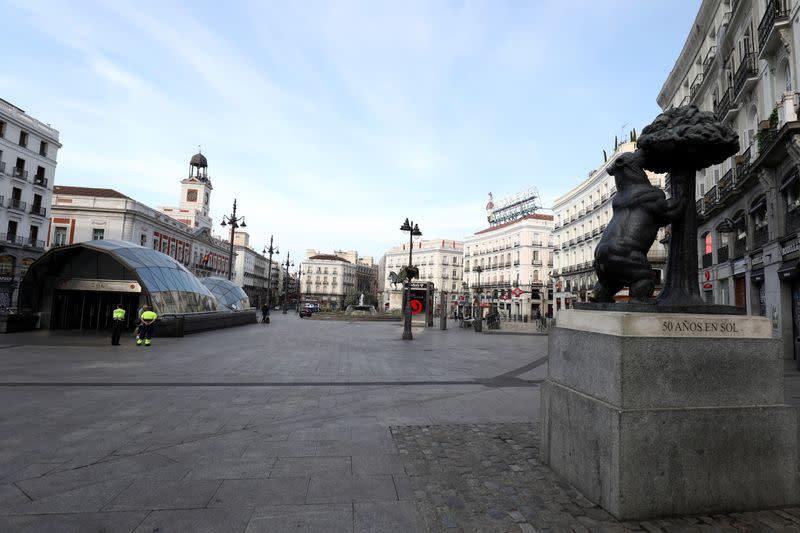 Workers stand in the empty Puerta de Sol square during partial lockdown, as part of a 15-day state of emergency to combat the coronavirus outbreak in Madrid