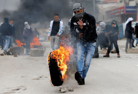 A Palestinian demonstrator kicks a burning tyre during clashes with Israeli troops in Halhoul, in the occupied West Bank February 17, 2018. REUTERS/Mussa Qawasma