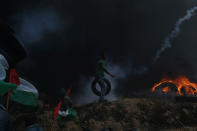 <p>A Palestinian demonstrator carries a tire as others take cover from Israeli fire and tear gas during a protest against the U.S. Embassy’s move to Jerusalem and ahead of the 70th anniversary of Nakba, at the Israel-Gaza border in the southern Gaza Strip on May 14, 2018. (Photo: Ibraheem Abu Mustafa/Reuters) </p>