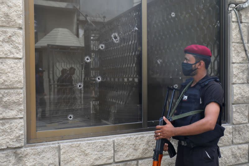 Police officer stands guard next to a bullet riddled window at the Pakistan Stock Exchange building after an attack in Karachi