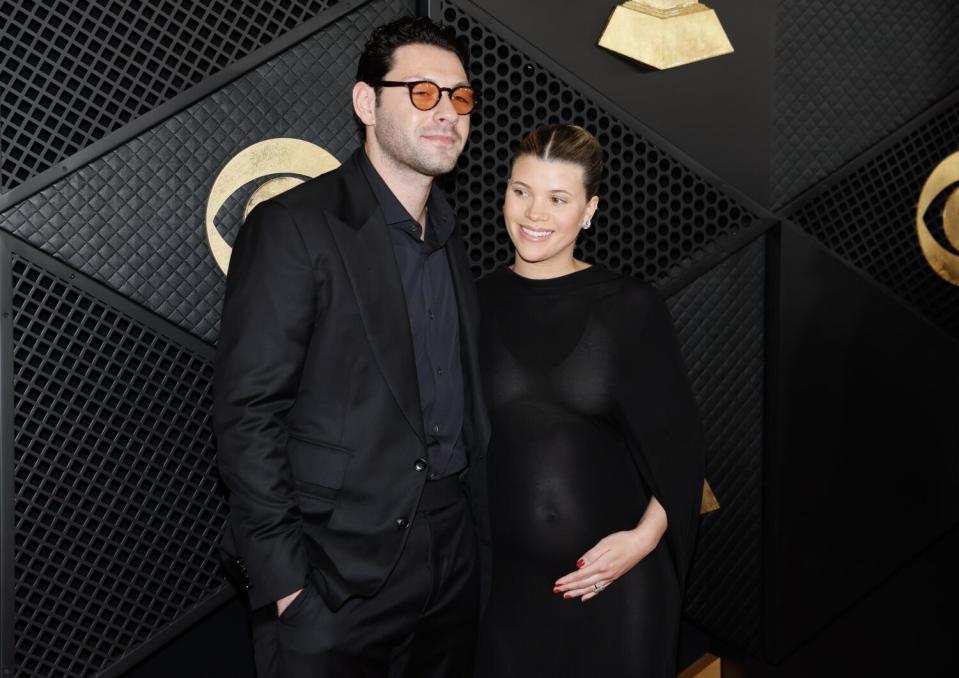 Elliot Grainge puts his arm around pregnant wife Sofia Richie Grainge. Both are wearing black.