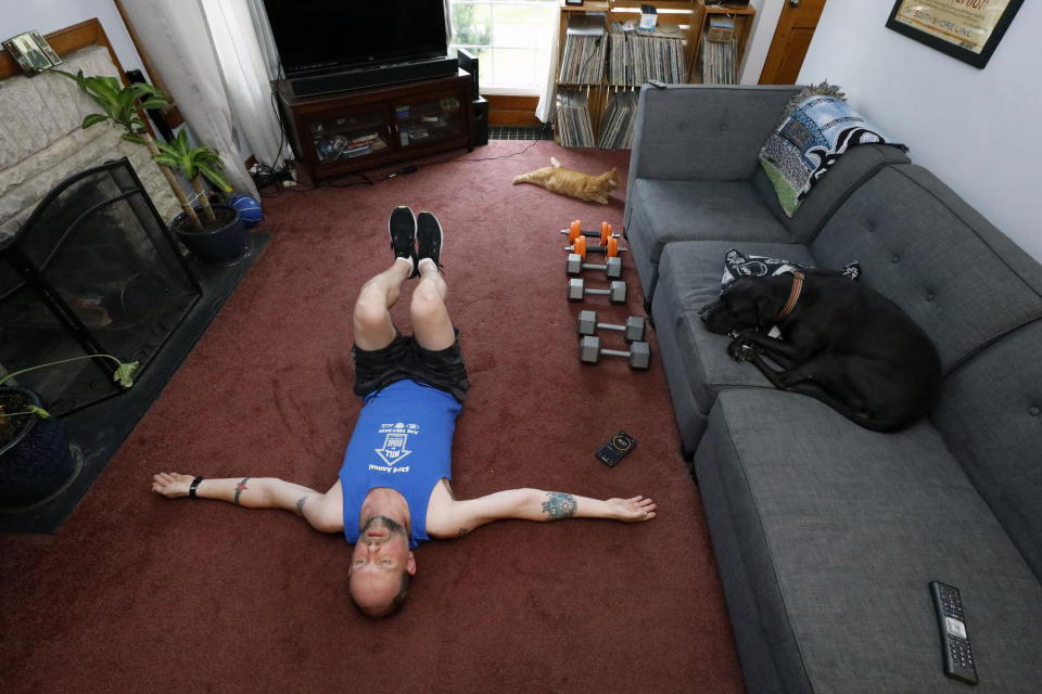 Christian Hainds stretches after his workout session as his dog, Reyna and cat, Oscar, lounge at his home in Hammond, Ind., Monday, June 7, 2021. Health officials have warned since early on in the pandemic that obesity and related conditions such as diabetes were risk factors for severe COVID-19. It wasn't until he was diagnosed as diabetic around the start of the pandemic that he felt the urgency to make changes. Hainds lost about 50 pounds during the pandemic, and at 180 pounds and 5 feet, 11 inches tall is no longer considered obese. (AP Photo/Shafkat Anowar)