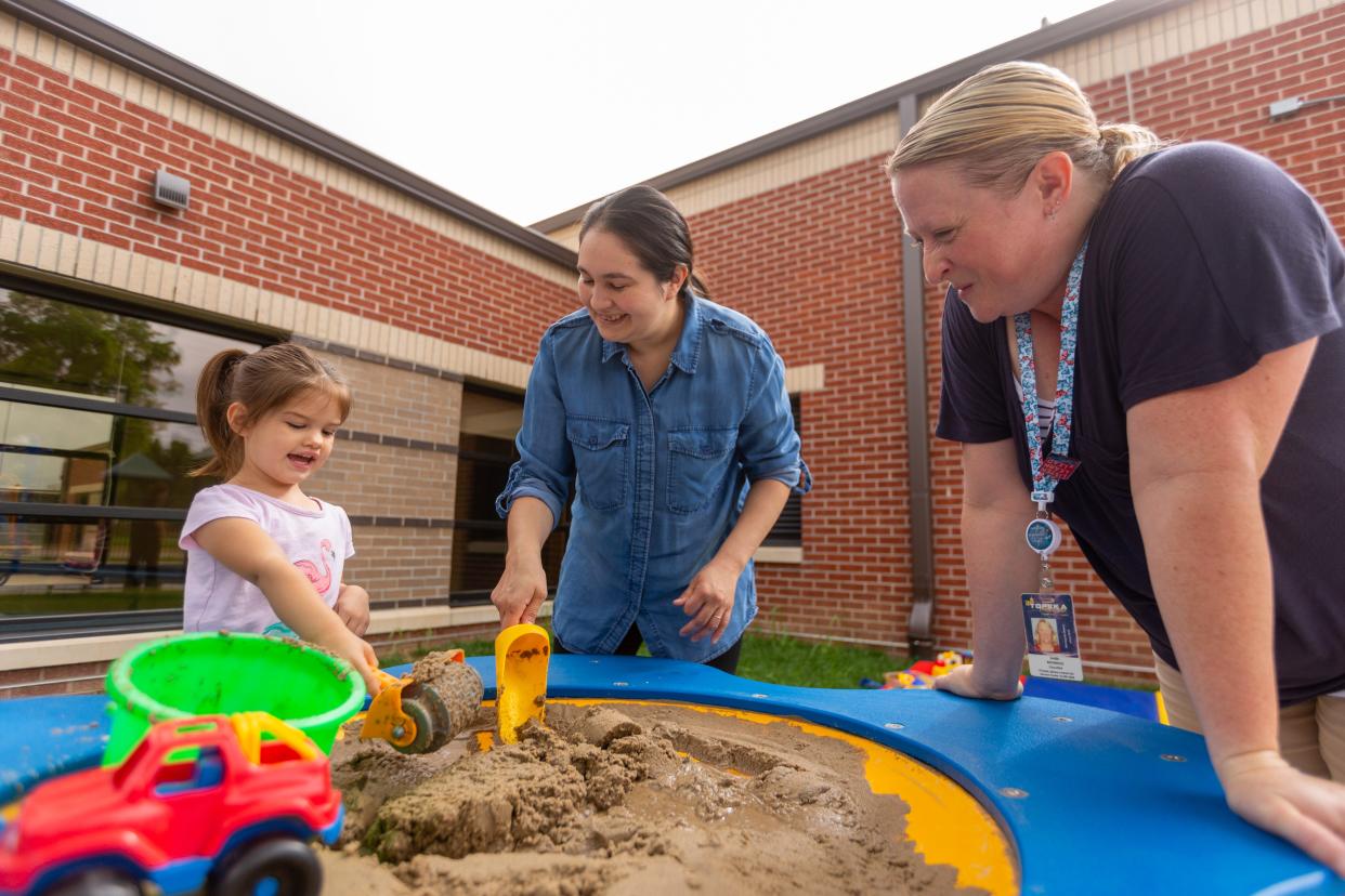 Topeka USD 501 Parents as Teachers educator Sheri Bounous, right, works with Blanca Cadogan and her daughter Ziva, 3, as they learn by playing with sand on the playground outside the Quinton Heights Education Center on Friday.