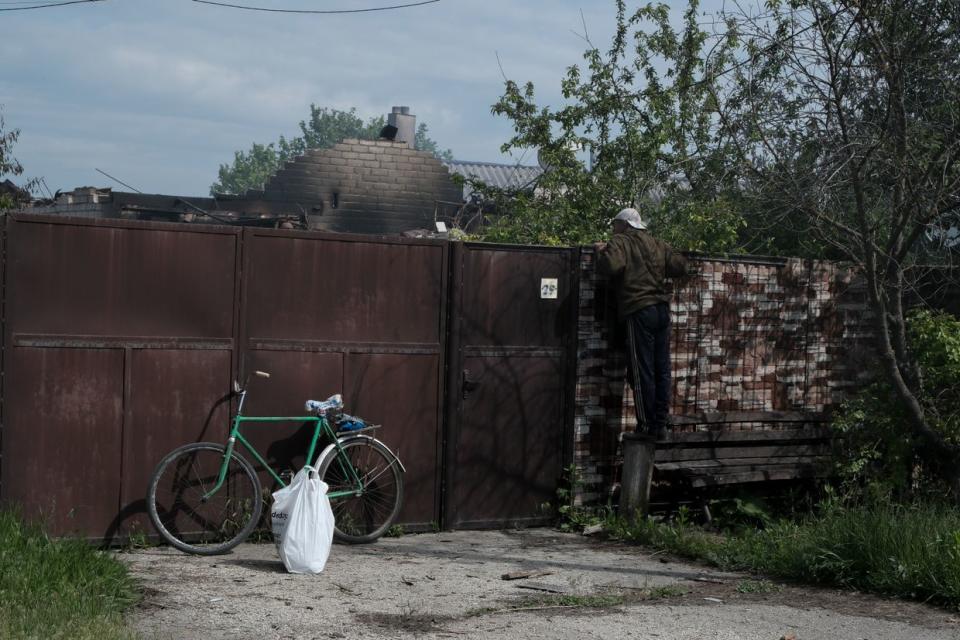 A local resident looks for a dog over the fence of a house destroyed by a Russian bomb in Vovchansk, Kharkiv Oblast, on May 11, 2024. (Francis Farrell/The Kyiv Independent)
