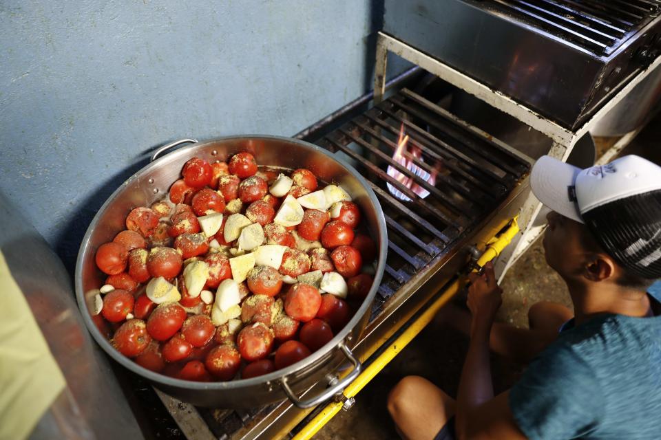 A migrant cooks a pot of tomatoes and onions at a shelter used mostly by Mexican and Central American migrants who are applying for asylum in the U.S., at the border in Tijuana, Mexico, Sunday, June 9, 2019. The mechanism that allows the U.S. to send migrants seeking asylum back to Mexico to await resolution of their cases has been running in Tijuana since January. (AP Photo/Eduardo Verdugo)