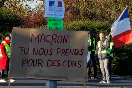 A man who holds French flag wears a yellow vest, a symbol of French drivers' nationwide protest against higher fuel prices, is seen on a roadblock near the entrance of the Paris-Brussels motorway in Cambrai, France, November 17, 2018. The placard reads "Macron you fool us". REUTERS/Pascal Rossignol