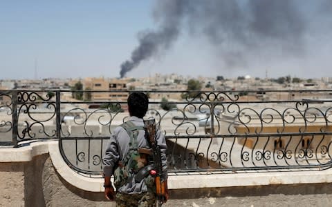 A Kurdish fighter from the People's Protection Units (YPG) looks at a smoke after an coalition airstrike in Raqqa - Credit: Reuters