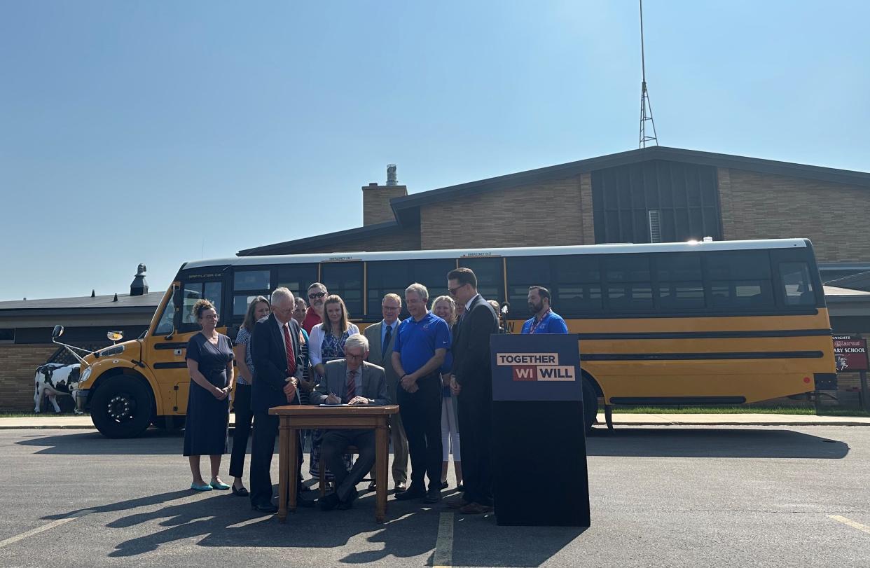 Democratic Gov. Tony Evers signs a bill allowing school board members to volunteer as bus drivers in New Glarus, surrounded by lawmakers and district officials.