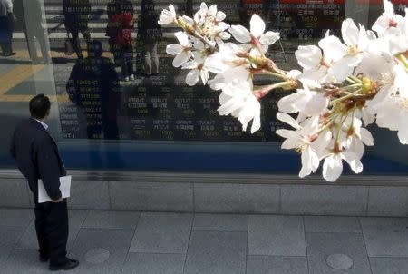 A Tokyo businessman looks at an electronic stock quotation board, as cherry blossoms bloom, outside a brokerage in Tokyo March 30, 2015. REUTERS/Issei Kato