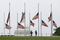 In this May 22, 2020 photo, people walk past American flags flying at half-staff at the Washington Monument in Washington. The pandemic is playing out in a divided country under a president who thrives on rousing his supporters and getting a rise out of those who don't like him, whether that means forgoing a mask, playing golf while millions hunker down or thrashing opponents on Twitter. (AP Photo/Patrick Semansky)