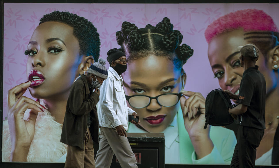 FILE - In this Monday, June 29, 2020, file photo, men in face masks walk past a hair product billboard on the street in Soweto, South Africa. The coronavirus pandemic has fractured global relationships as governments act in the interest of their citizens first, but John Nkengasong, Africa's top public health official, has helped to steer the continent's 54 countries into an alliance praised as responding better than some richer nations. (AP Photo/Themba Hadebe, File)