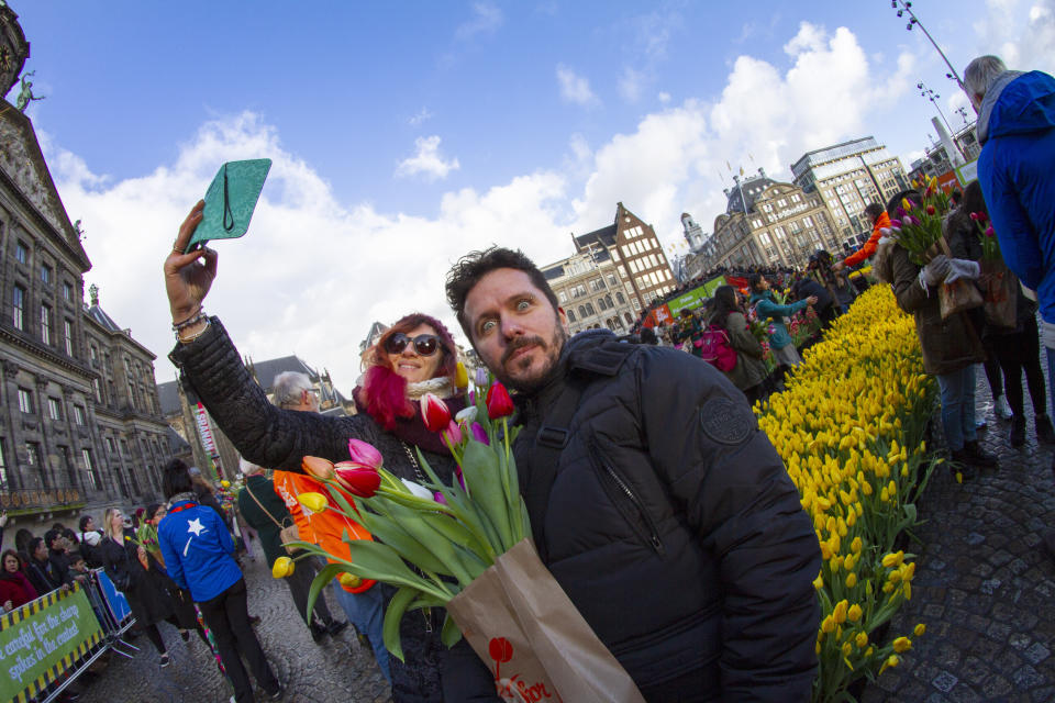 A couple takes a selfie as scores of people pick free tulips on Dam Square in front of the Royal Palace in Amsterdam, Netherlands, Saturday, Jan. 18, 2020, on national tulip day which marks the opening of the 2020 tulip season. (AP Photo/Peter Dejong)