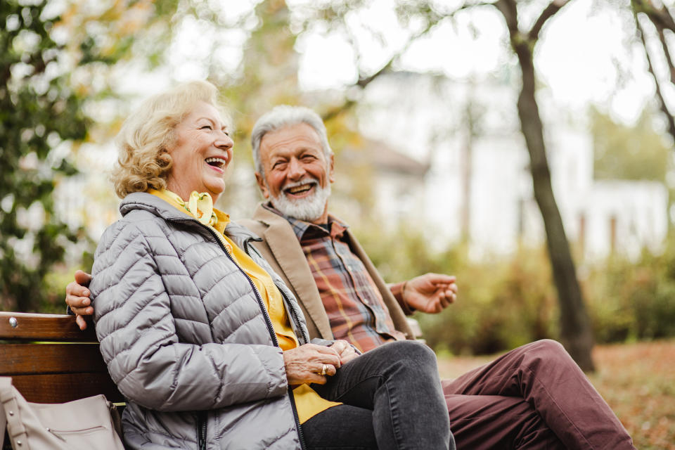 A happy senior couple sitting on a bench together in warm clothing. Seniors can stay healthy this fall and winter with updated vaccines and fall prevention strategies. (Getty)