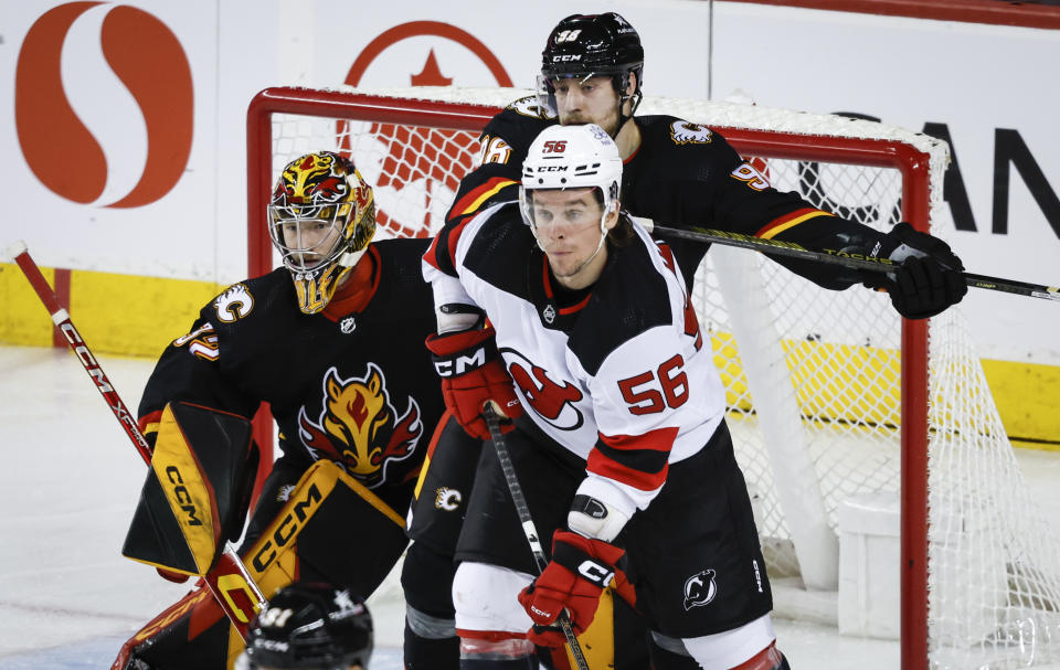 New Jersey Devils forward Erik Haula, right, is pushed away from Calgary Flames goalie Dustin Wolf, left, by defenseman Ilya Solovyov during the third period of an NHL hockey game Saturday, Dec. 9, 2023, in Calgary, Alberta. (Jeff McIntosh/The Canadian Press via AP)