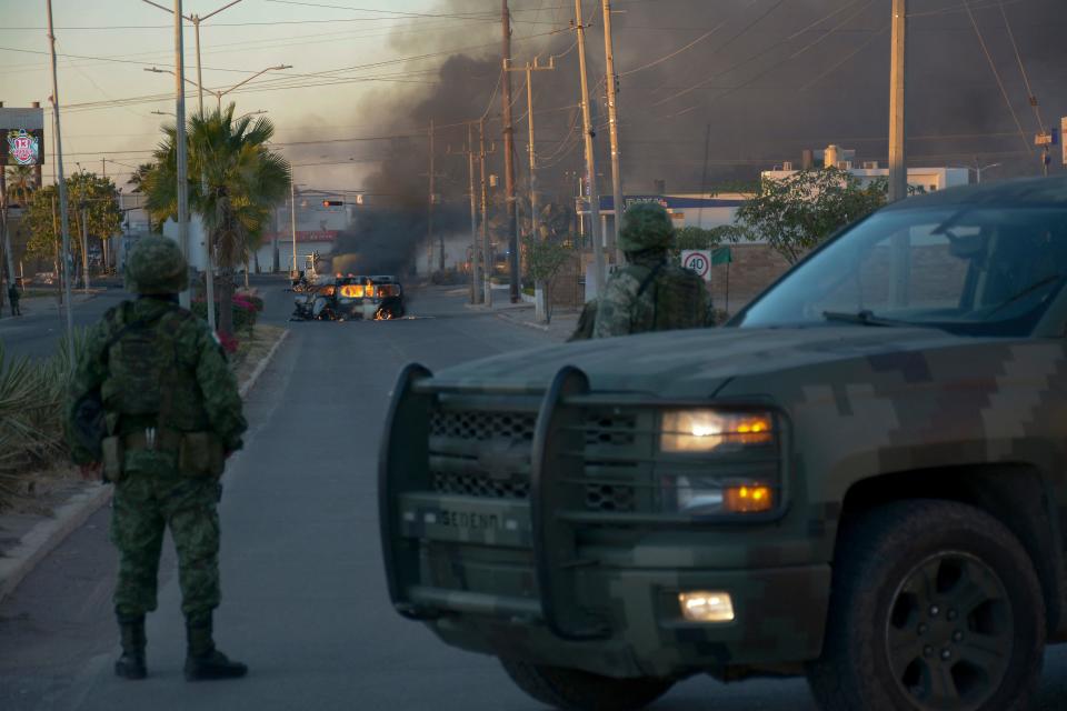 Mexicans soldiers stand guard near burning vehicles on a street during an operation to arrest the son of Joaquin 