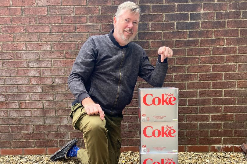 Man kneeling pointing at stack of boxes of Diet Coke