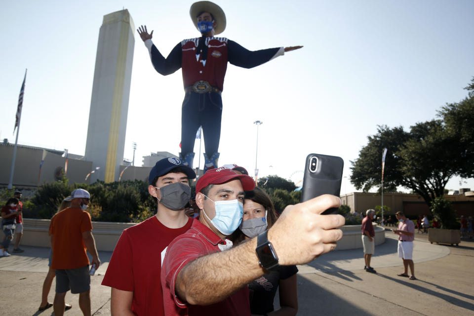 Oklahoma fans Lucas Aleman, Josias Aleman and Annie Aleman, of Kansas City, take a selfie in front of "Big Tex" prior to an NCAA college football game between University of Texas and Oklahoma. in Dallas, Saturday, Oct. 10, 2020. (AP Photo/Michael Ainsworth)