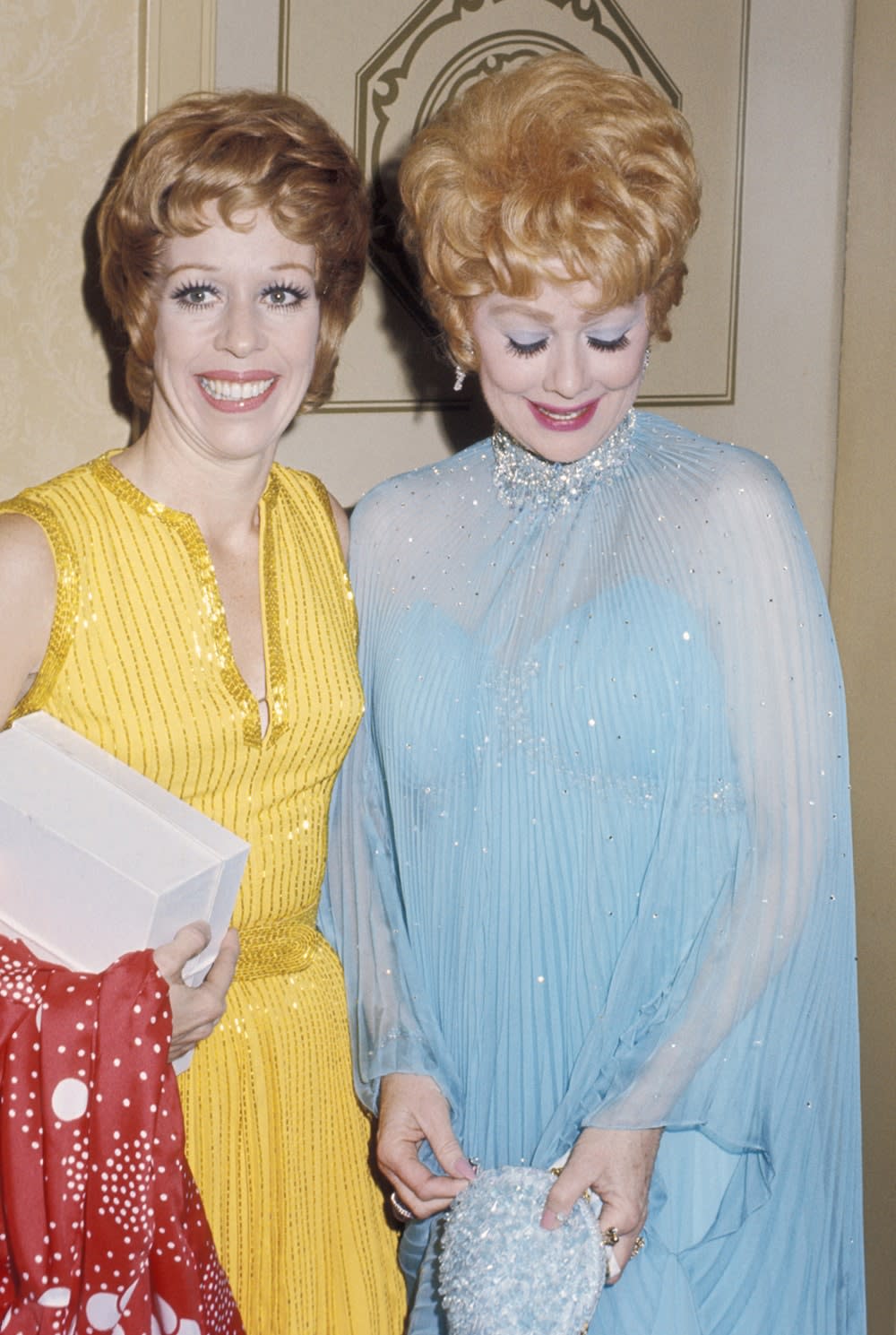 Carol Burnett wearing a yellow dress next to Lucille Ball wearing a blue dress