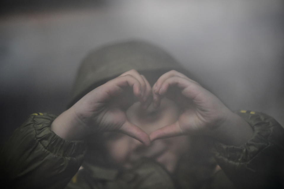 A child fleeing from Ukraine makes a heart shape with her hands while waiting for a train.