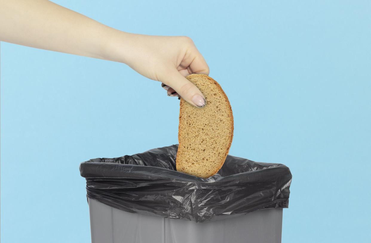 throwing a piece of bread into the trash can, bread in hand in front of the trash can, stale food concept. rejection of flour products