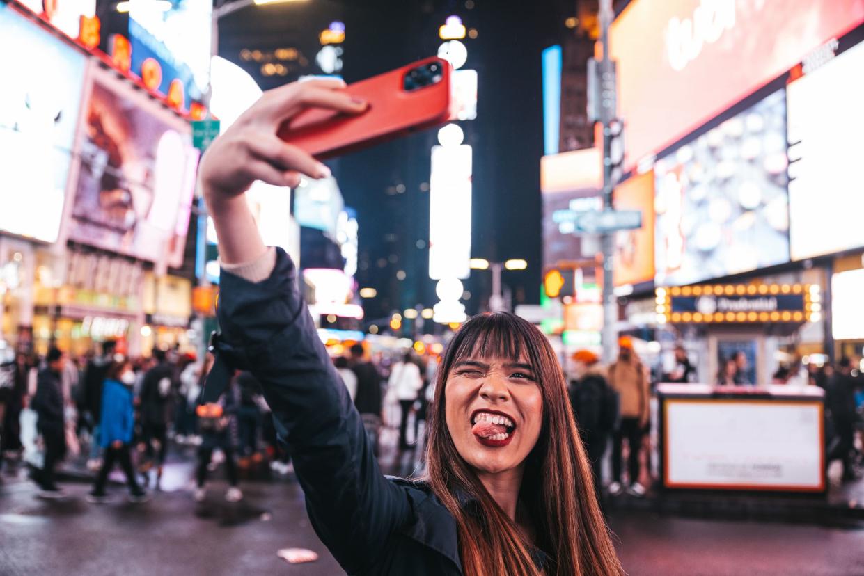 Midtown New York, young Taiwanese tourist woman  spending a night in Times Square and sharing on social media with her smart phone.