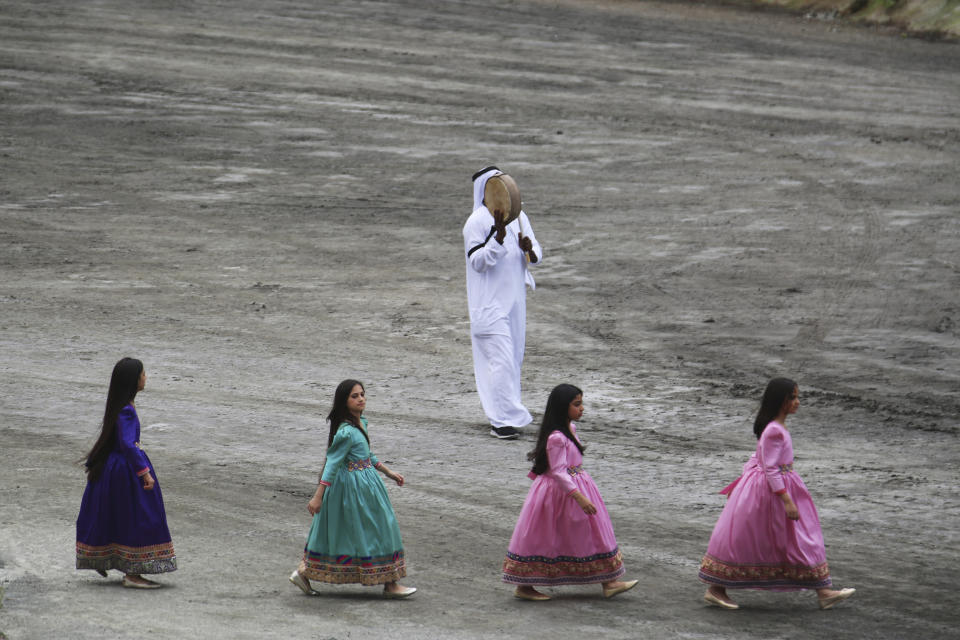 Young girls walk past an Emirati man playing a traditional drum at the opening ceremony of the International Defense Exhibition and Conference in Abu Dhabi, United Arab Emirates, Sunday, Feb. 17, 2019. The biennial arms show in Abu Dhabi comes as the United Arab Emirates faces increasing criticism for its role in the yearlong war in Yemen. (AP Photo/Jon Gambrell)