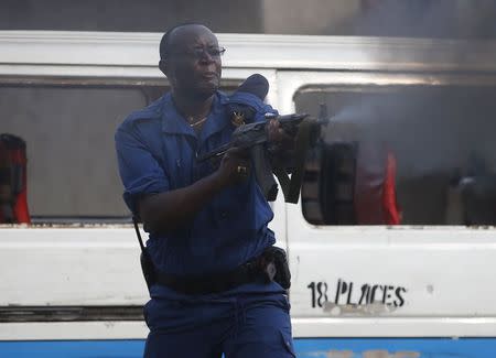 A policeman fires his AK-47 rifle as protesters throw stones during a protest against Burundi President Pierre Nkurunziza and his bid for a third term in Bujumbura, Burundi, May 26, 2015. REUTERS/Goran Tomasevic