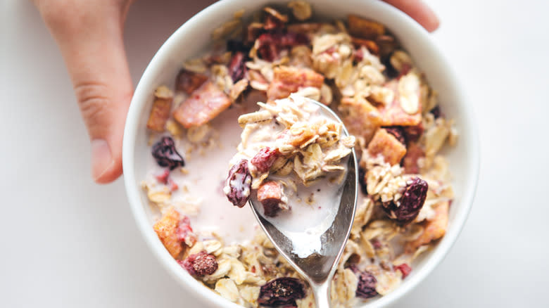 Scooping overnight oats from bowl with fruit and milk