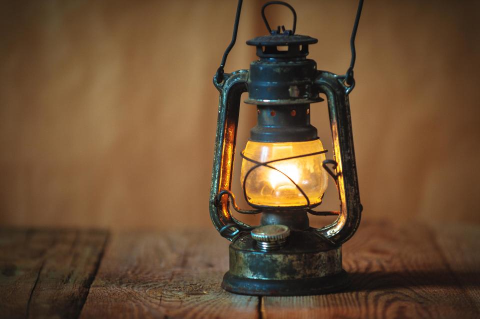 vintage kerosene oil lantern lamp burning with a soft glow light in an antique rustic country barn with aged wood floor
