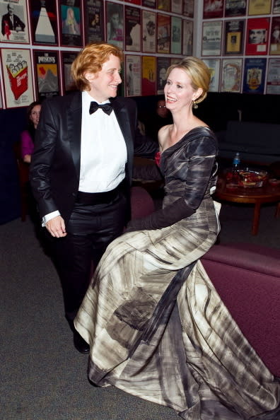 Christine Marinoni in a tuxedo and Cynthia Nixon in an elegant gown are smiling at each other at a theater event