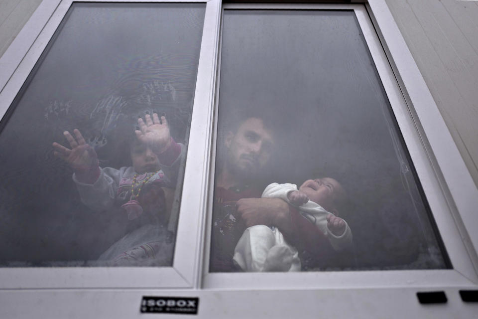 FILE - In this Wednesday, Dec. 28, 2016 file photo, refugee Siban Assad, 20, from al-Hasaka, Syria, looks out from the window of his shelter while holding his daughters, Ruba, one month, and Maldar, 1, at the Ritsona , Greece, refugee camp, about 86 kilometers (53 miles) north of Athens. Despite the rhetoric about migration crises in Europe and the U.S., the top three countries taking in refugees are Turkey, Pakistan and Uganda. Germany comes in a distant fifth. (AP Photo/Muhammed Muheisen)
